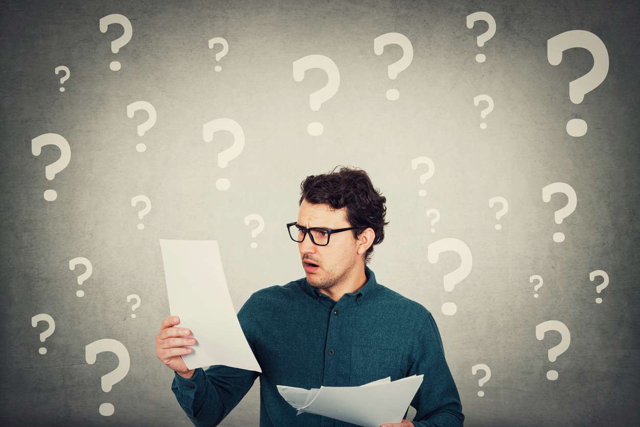 Perplexed man looking stunned and dazed at paper documents. Confused business person in trouble as holds different sheets with negative financial reports. Frightened guy, question marks over head.